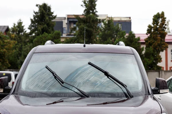 Car wipers cleaning water drops from windshield glass outdoors