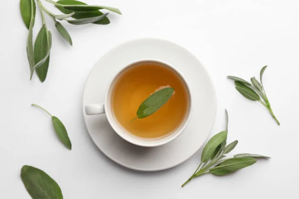 Cup of aromatic herbal tea with sage on white table, flat lay
