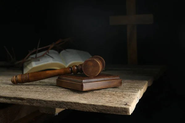 Judge gavel, bible, cross and crown of thorns on wooden table against black background