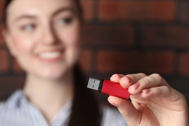 Kadın USB belleği tuğla duvarın yanında tutuyor, eline odaklan.