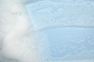 Açık mavi arka planda beyaz yıkama köpüğü, üst görünüm