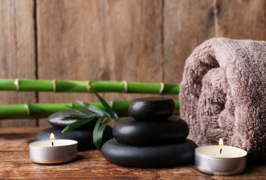 Tahta masaya istiflenmiş spa taşları, bambu, mumlar ve havlu. Metin için boşluk