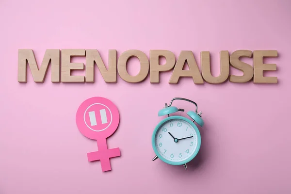 stock image Word Menopause made of wooden letters, female gender sign and alarm clock on pink background, flat lay