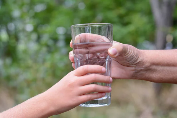 Child giving glass of water to elderly woman outdoors, closeup