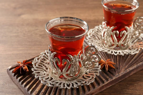 Glasses of traditional Turkish tea in vintage holders and anise stars on wooden table, closeup