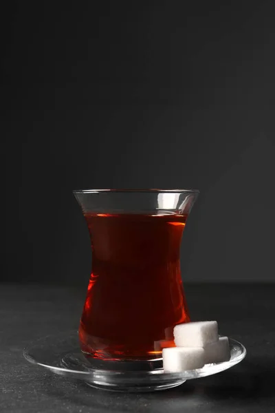 Glass with traditional Turkish tea and sugar cubes on black table