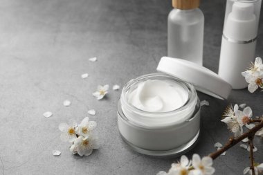 Yüz kremi kavanozu ve gri masadaki diğer kozmetik ürünler. Metin için boşluk