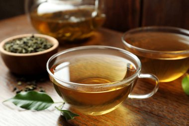 Cam bardaklarda taze yeşil çay ve ahşap masada yapraklar.