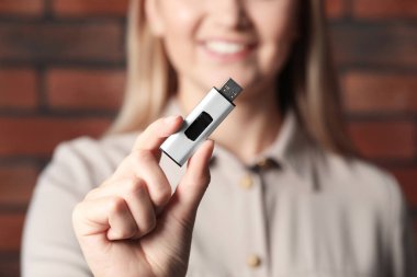 Kadın USB belleği tuğla duvarın yanında tutuyor, eline odaklan.