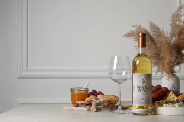 Bir şişe beyaz şarap, bardak ve atıştırmalıklar masada, mesaj için yer var.