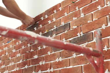 Profesyonel müteahhit duvara dekoratif tuğla yapıştırıyor, yakın plan. Döşeme kurulum süreci