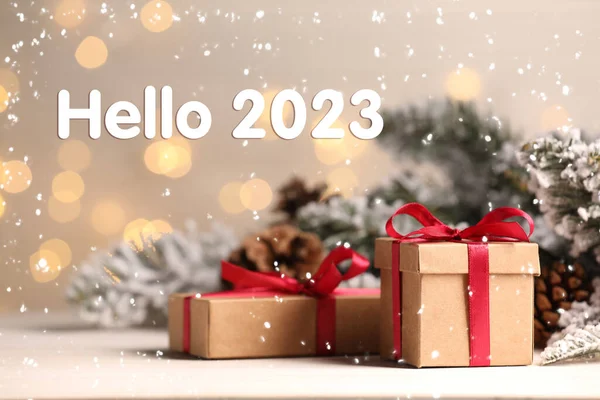 Hello 2023. Gift boxes and Christmas decor on wooden table against blurred festive lights