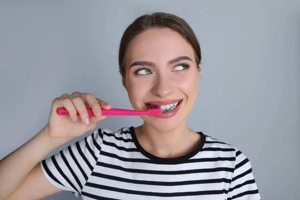 Young woman brushing teeth with charcoal toothpaste on grey background