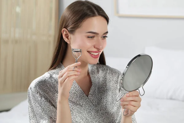Woman with eyelash curler near mirror at home