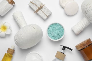 Beyaz arka planda bitkisel masaj torbaları ve farklı bakım ürünleriyle güzel bir spa kompozisyonu.
