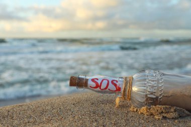 Deniz kenarındaki kumda SOS mesajı olan cam şişe, yakın plan.