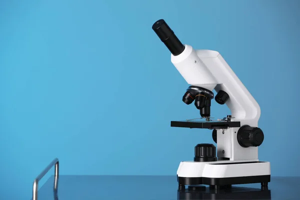 Modern microscope on metal table against blue background. Space for text