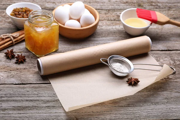 Roll of baking parchment paper, different ingredients and kitchen tools on wooden table