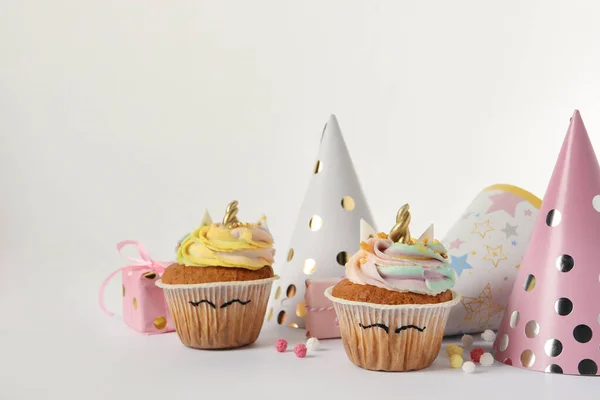 Cute sweet unicorn cupcakes and party hats on white background, space for text