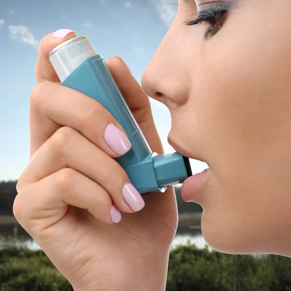 Woman using asthma inhaler, closeup. Emergency first aid during outdoor recreation