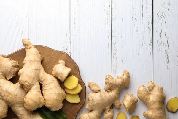 Cut and whole fresh ginger with leaves on white wooden table, flat lay. Space for text