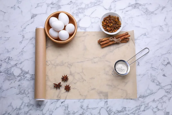 Roll of baking parchment paper and different ingredients on white marble table, flat lay. Space for text
