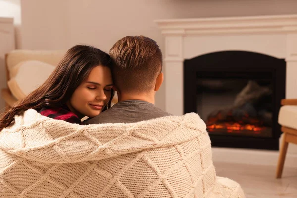 Lovely couple wrapped in blanket near fireplace at home, back view