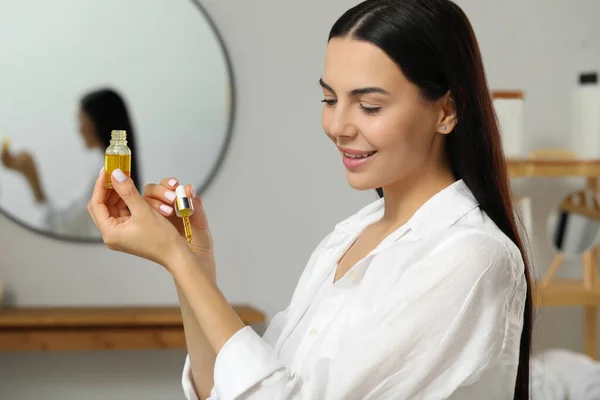 Young woman applying essential oil on wrist indoors