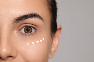 Göz altı kremi sürmüş genç bir kadın açık gri arka planda, yakın plan. Metin için boşluk