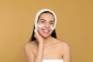 Mutlu genç kadın bej arka planda kozmetik ürünlerle yüzünü yıkıyor.