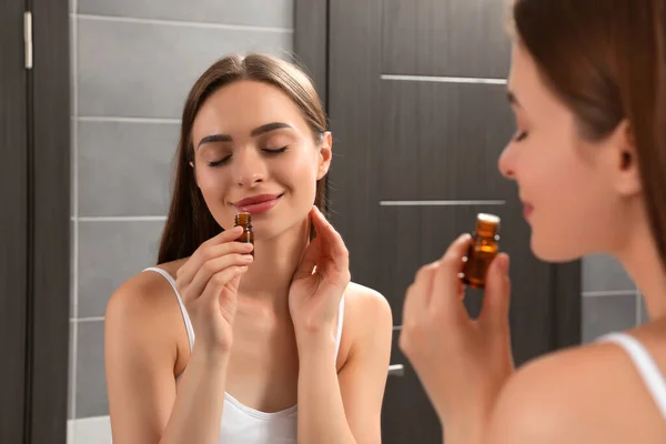 Young woman smelling essential oil in bathroom