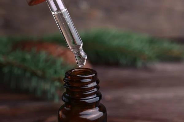 Dripping pine essential oil into bottle at wooden table, closeup