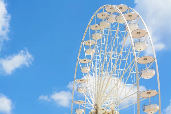 Large white observation wheel against blue cloudy sky, space for text