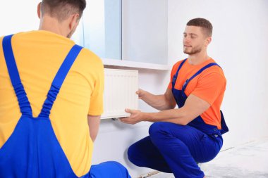 Professional plumbers installing new heating radiator in room