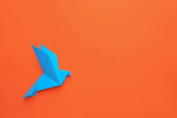 Beautiful light blue origami bird on orange background, top view. Space for text