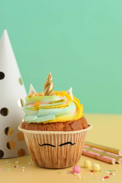 Cute sweet unicorn cupcake and party items on yellow table