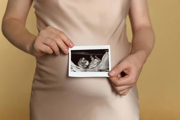 Pregnant woman with ultrasound picture of baby on beige background, closeup