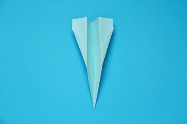 Paper plane on light blue background, top view