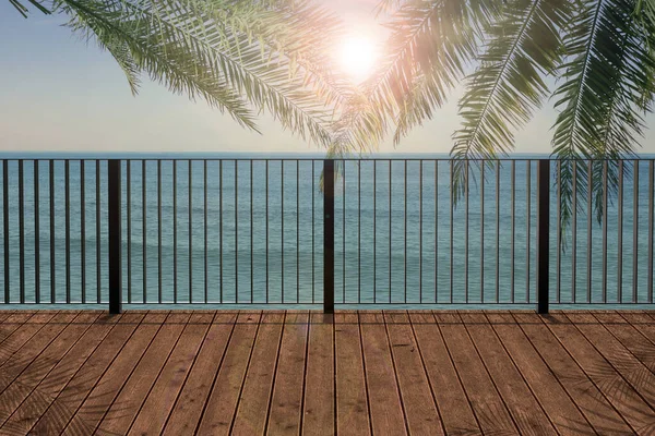 Outdoor wooden terrace under palm trees revealing picturesque view on ocean in morning