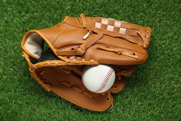 Catcher\'s mitt and baseball ball on green grass, top view. Sports game