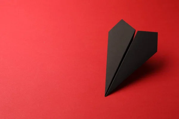 Handmade black paper plane on red background, space for text