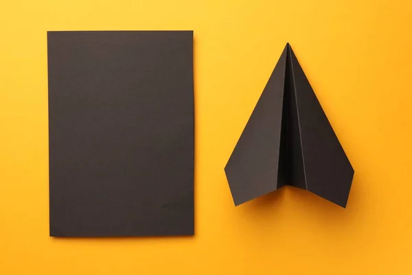 Handmade black plane and piece of paper on yellow background, flat lay
