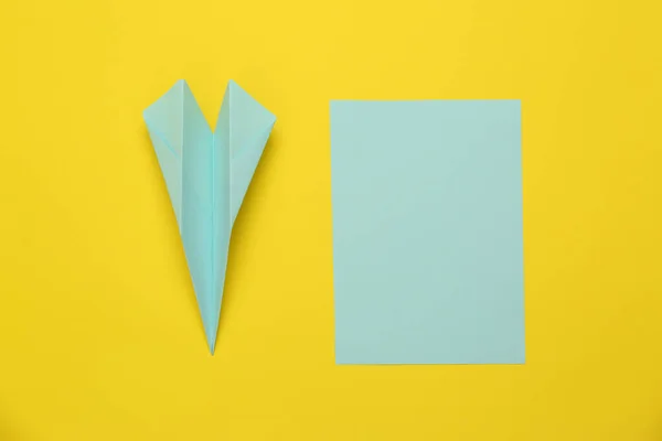Handmade light blue plane and piece of paper on yellow background, flat lay