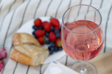 Glass of delicious rose wine and food on white picnic blanket, closeup