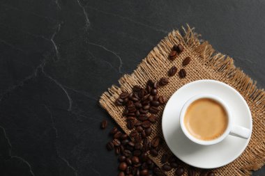 Bir fincan sıcak aromatik kahve ve kavrulmuş fasulye, siyah masada, düz yerde. Metin için boşluk