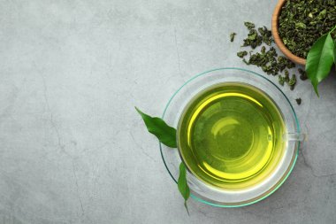 Taze yeşil çay fincanda çay, çay tabağı ve kuru yapraklar gri masada, düz yerde. Metin için boşluk