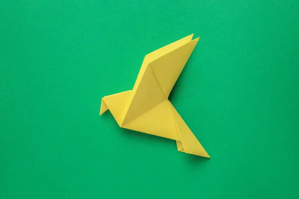 Beautiful yellow origami bird on green background, top view