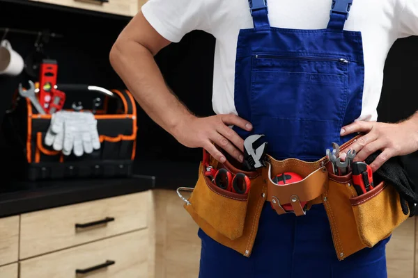 Professional plumber with tool belt indoors, closeup