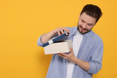 Mutlu adam hediyesini turuncu arka planda açıyor. Metin için boşluk