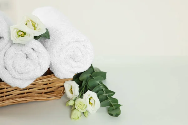 Soft folded towels and flowers on white table, space for text